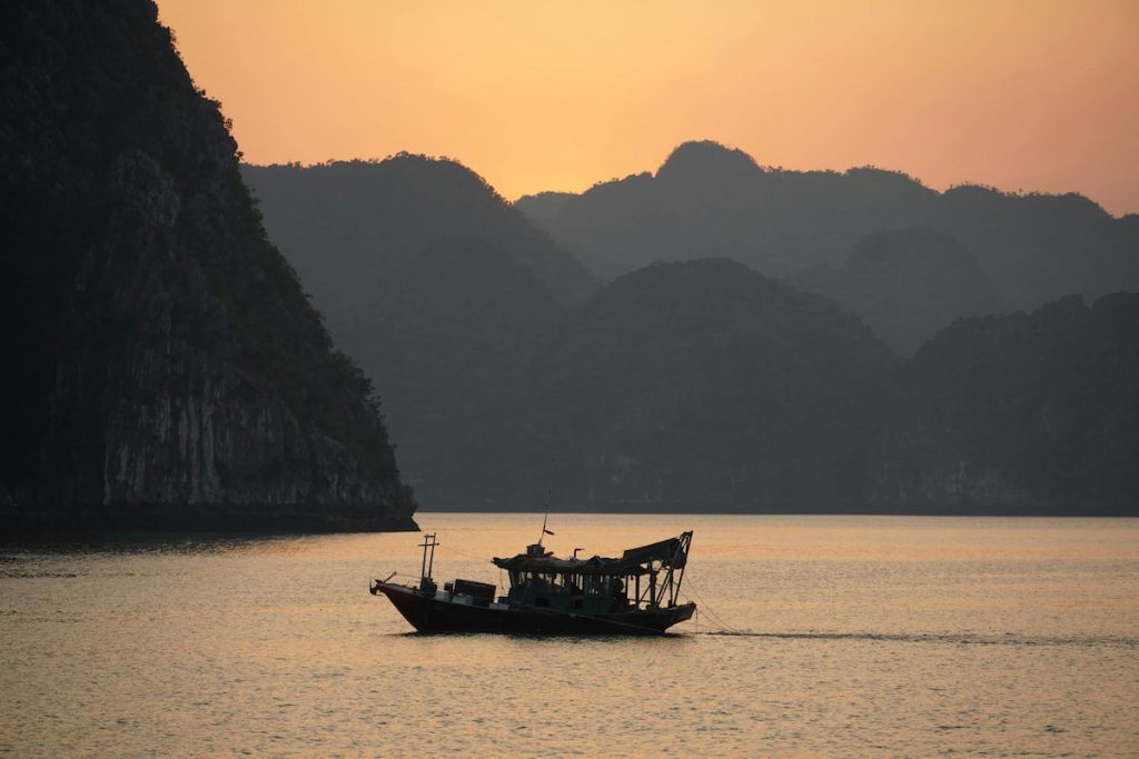 Juncos tradicionales navegando entre las torres de caliza de la Bahía de Halong al atardecer